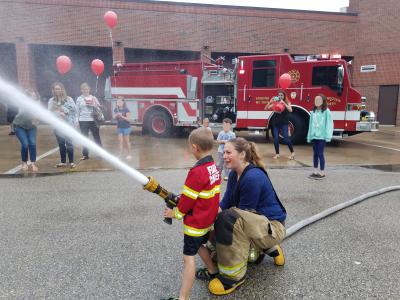 Fire Fighter Helping Child Spray Hose